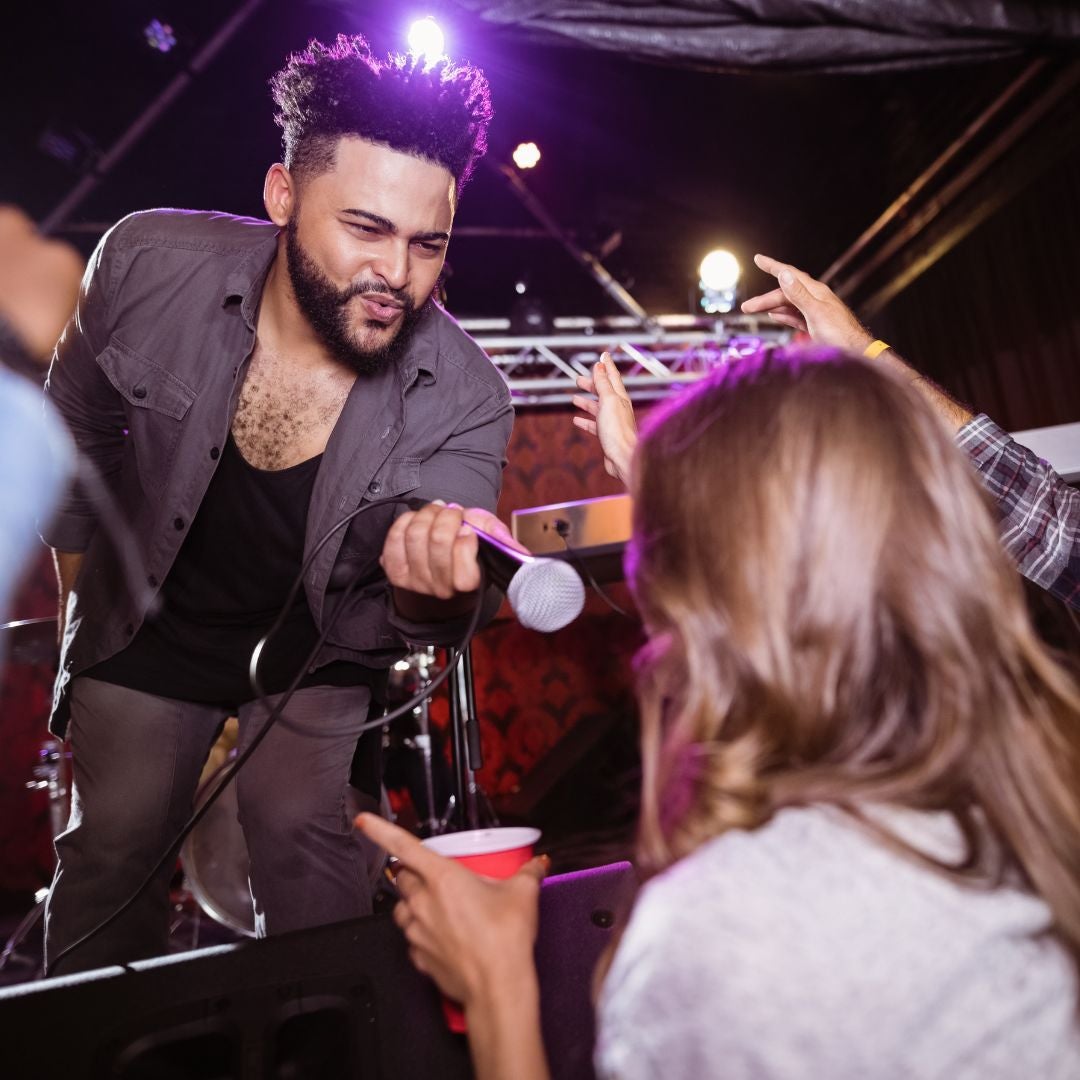 musician handing a microphone to a woman in the audience of a concert